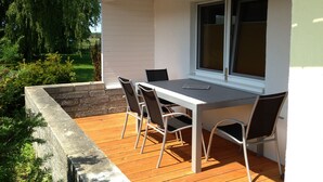 Eine Terrasse mit Tisch und Stühlen, einem Fenster und Blick auf die umliegende Grünfläche.