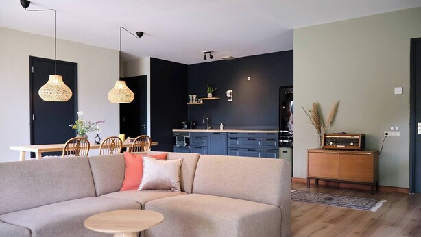 A modern living room with a sectional sofa, a dining table, and a kitchen area in the background.