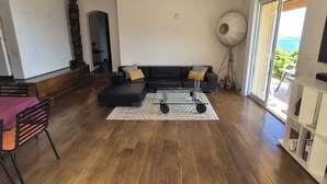 A spacious living room with a black sofa, a glass coffee table, and a large floor lamp. There is a sliding glass door leading to a balcony with a view of the sea. - Bella vista (Santa-Maria-di-Lota)