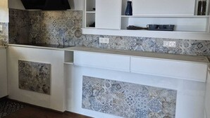 A kitchen with patterned tiles, white cabinets, and a black range hood. - Bella vista (Santa-Maria-di-Lota)