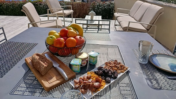 A table with fruits, nuts, bread, and yogurt, set on a terrace with a view of the sea and buildings. - Bella vista (Santa-Maria-di-Lota)