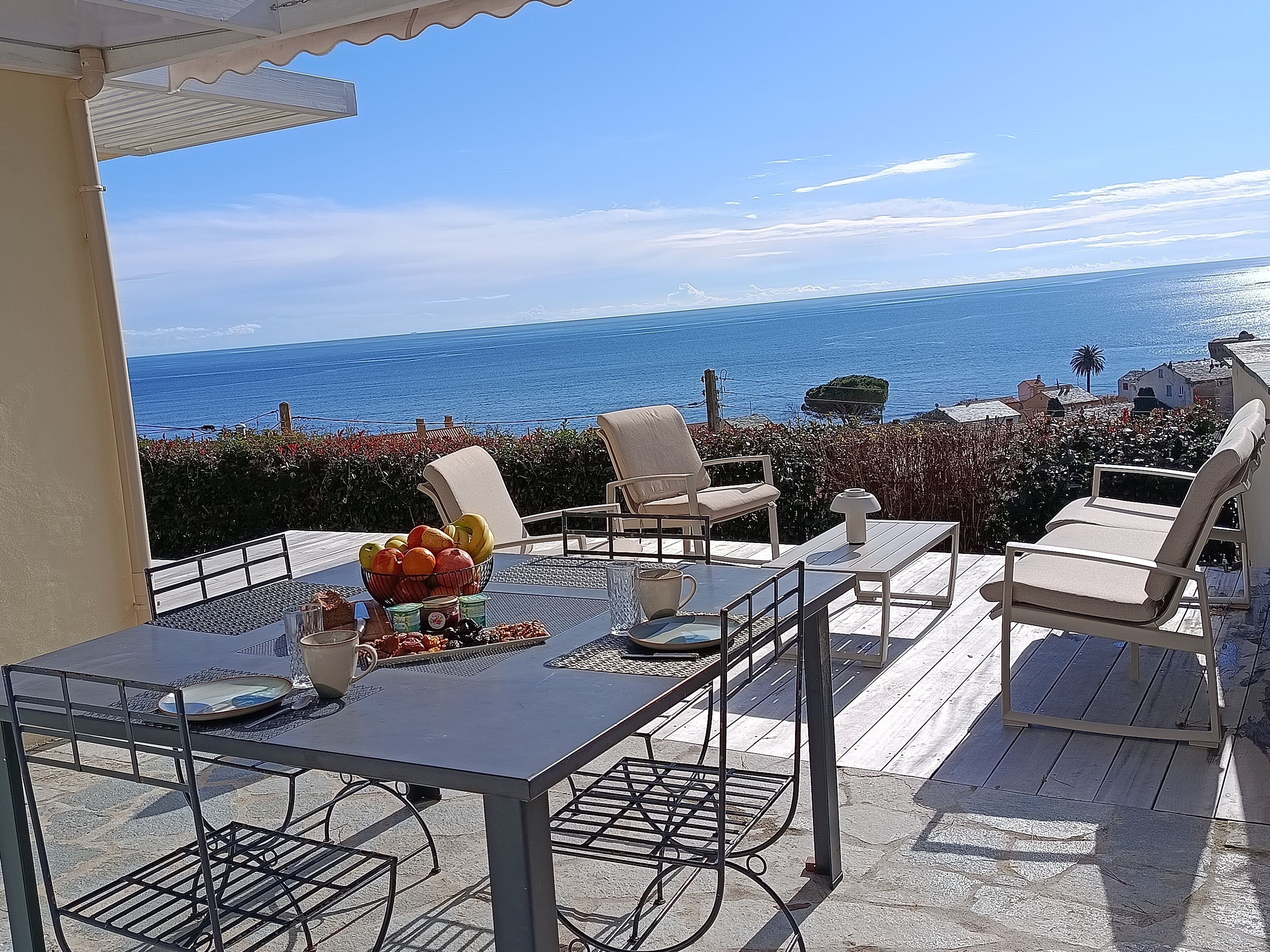 A terrace with a table set for dining, overlooking a coastal view.