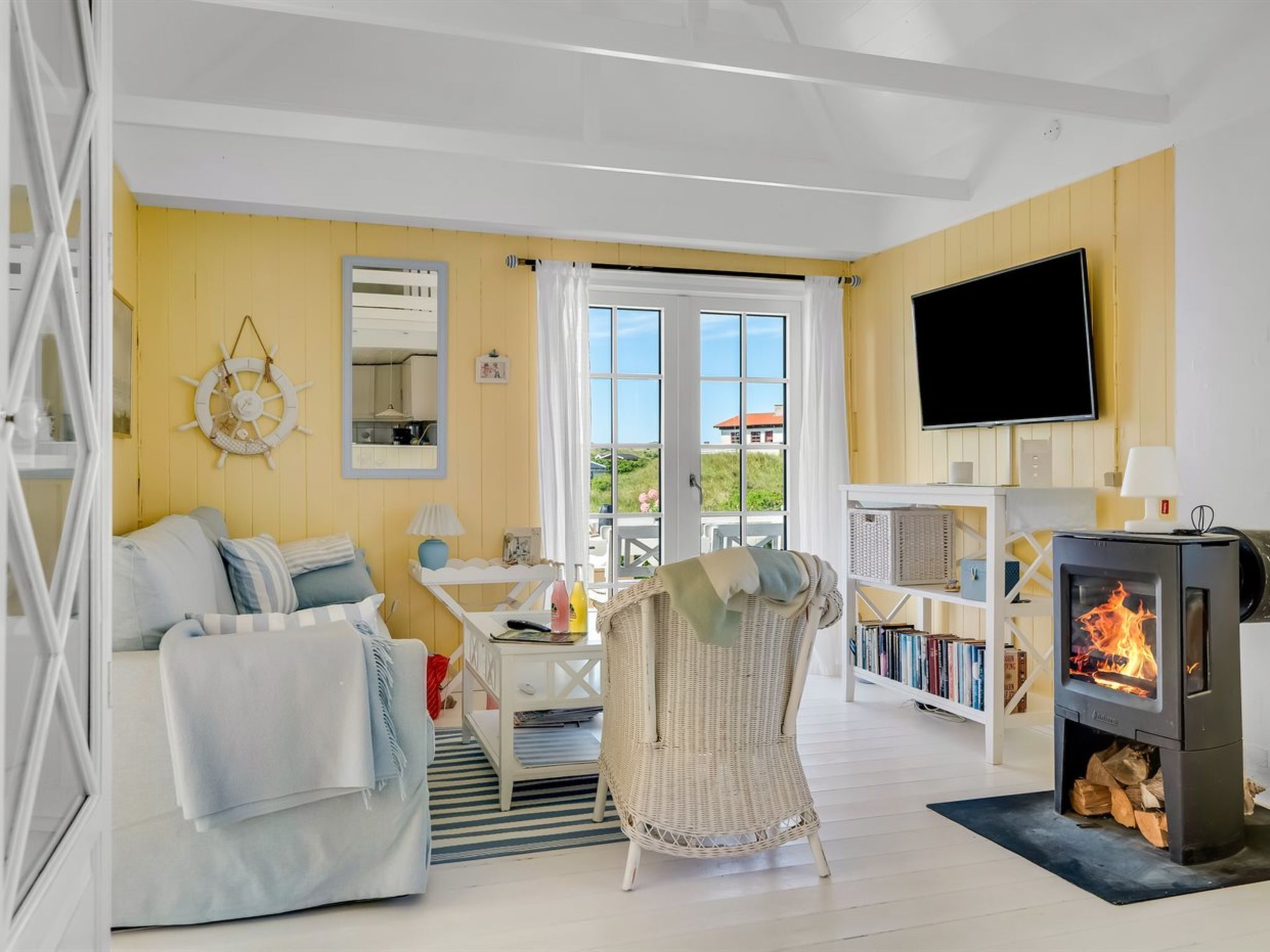 Een gezellige woonkamer met een bank, een rieten fauteuil, een open haard, een televisie en een raam met uitzicht.