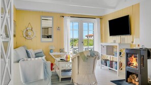 Uma sala de estar aconchegante com um sofá, uma poltrona de vime, lareira, televisão e janela com vista.