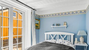 Quarto com cama, mesa de cabeceira, luminária, janela com cortinas e parede com moldura decorativa.