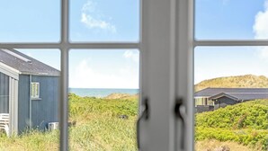 Vista pela janela com paisagem costeira, incluindo um edifício e vegetação.
