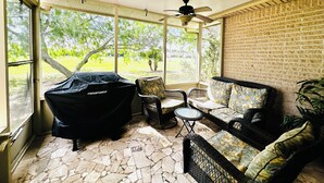 Uma área de varanda coberta com ventilador de teto, móveis de exterior e churrasqueira.