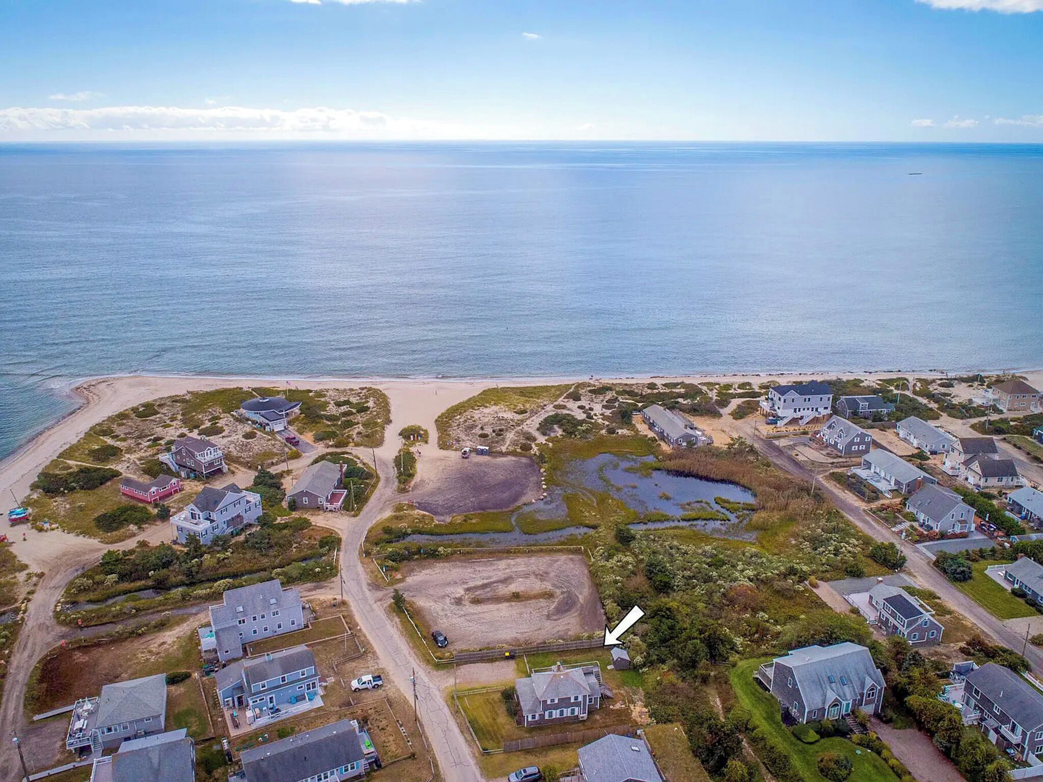 An aerial view of a coastal residential area with houses, a beach, and a large body of water.