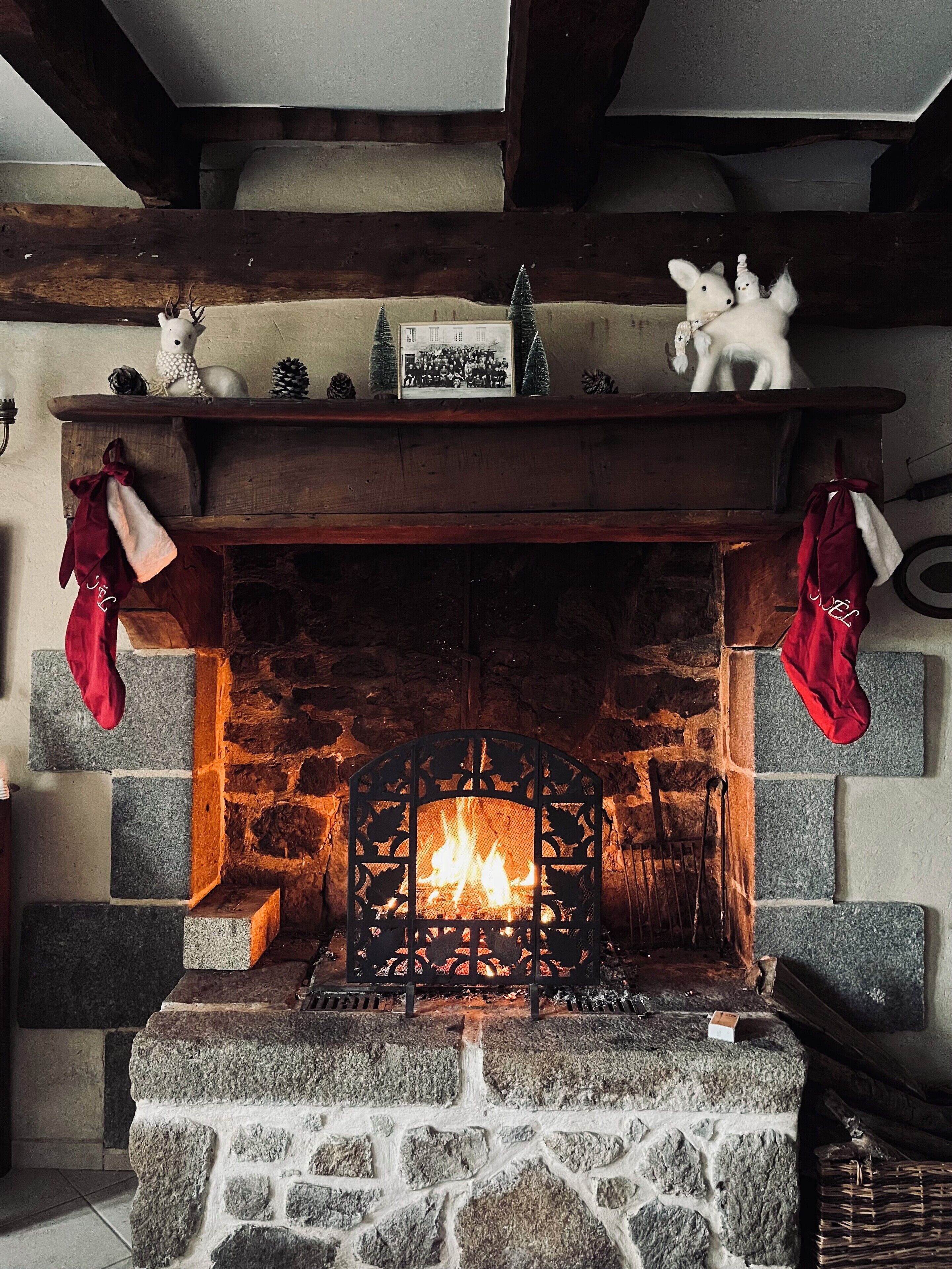 Una chimenea de piedra con fuego, flanqueada por calcetines rojos, y una repisa superior con objetos decorativos.