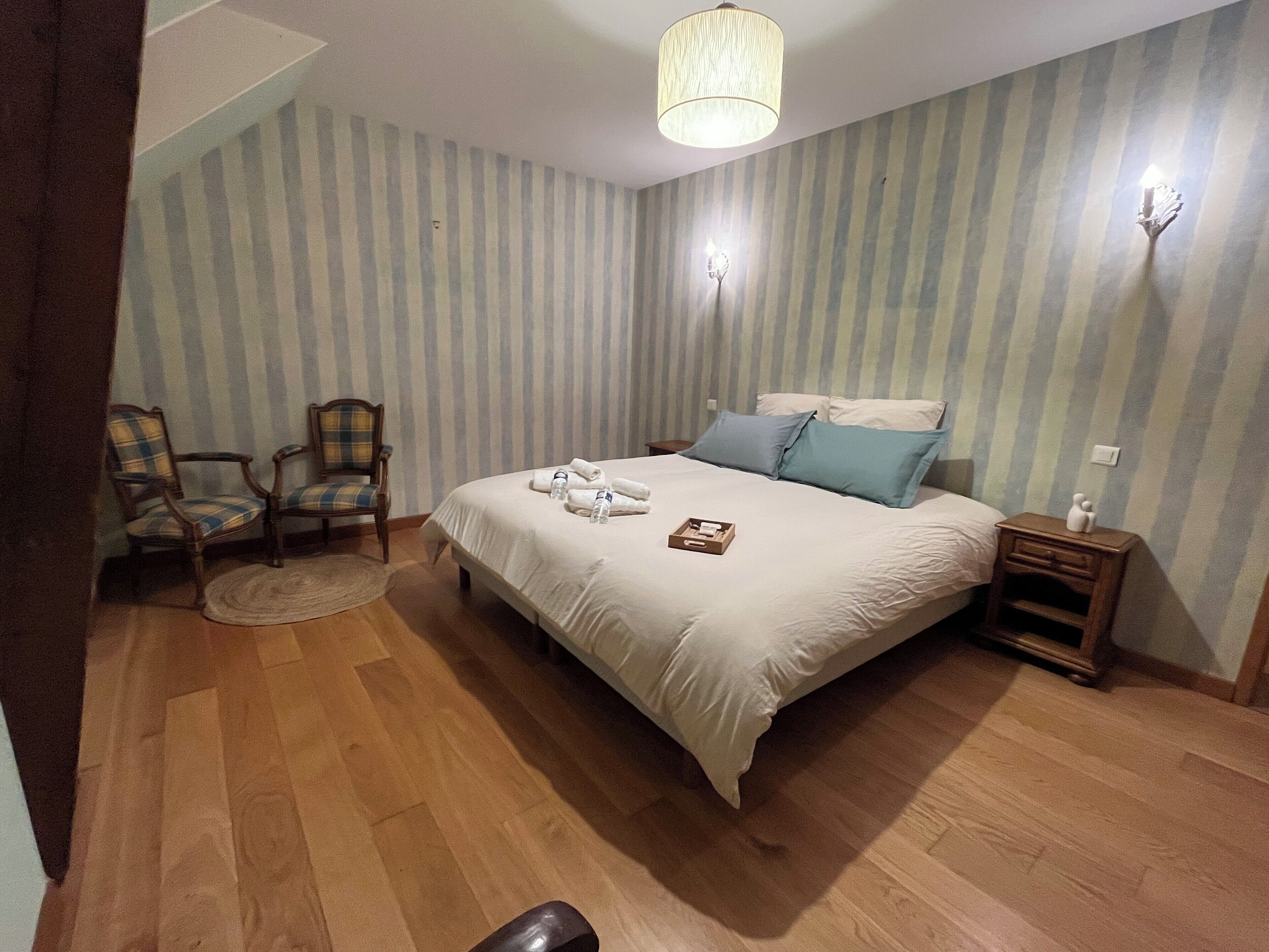 Un dormitorio con una cama grande, dos sillas, una mesita de noche y una lámpara.