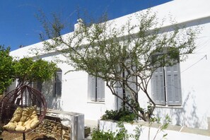 A white building with shutters, a hanging chair, and a tree.