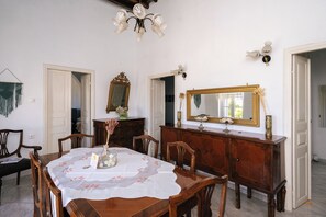 A dining room with a table set for four, a wooden cabinet, two wall-mounted mirrors, and a chandelier.
