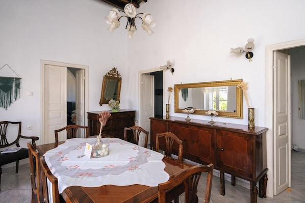 Comedor con una mesa dispuesta para cuatro, un aparador de madera, dos espejos en la pared y una lámpara de araña.