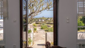 Une pièce dotée d’une grande fenêtre, offrant une vue sur un paysage côtier, et comprenant une petite table sur laquelle est posé un vase.
