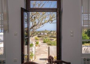 A room with a large window, a view of a coastal landscape, and a small table with a vase.