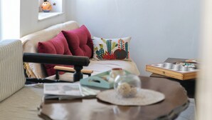 Un salon chaleureux avec un canapé, une table basse, un jeu de société et une fenêtre décorée d’un cactus.