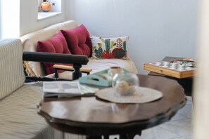 Un salon chaleureux avec un canapé, une table basse, un jeu de société et une fenêtre décorée d’un cactus.