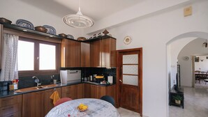 A kitchen with wooden cabinets, a built-in oven, a dining table with chairs, and a decorative ceiling light. - Kypseli House - Quiet Garden Home for Families & Groups, steps from Apollonia (Apollonia)