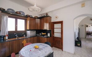 A kitchen with wooden cabinets, a built-in oven, a sink, and a dining area with a table and chairs. - Kypseli House - Quiet Garden Home for Families & Groups, steps from Apollonia (Apollonia)