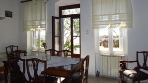A dining area with a table set for four, wooden chairs, a chandelier, and large windows with curtains. - Kypseli House - Quiet Garden Home for Families & Groups, steps from Apollonia (Apollonia)
