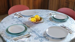 Une table de salle à manger ronde, recouverte d’une nappe à motifs floraux, entourée de quatre chaises, et un saladier rempli de citrons placé au centre.