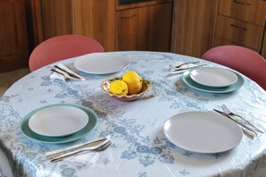 Une table de salle à manger ronde, recouverte d’une nappe à motifs floraux, entourée de quatre chaises, et un saladier rempli de citrons placé au centre.