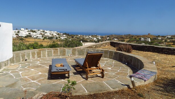 A stone patio with lounge chairs and a table overlooking a coastal village. - Kypseli House - Quiet Garden Home for Families & Groups, steps from Apollonia (Apollonia)