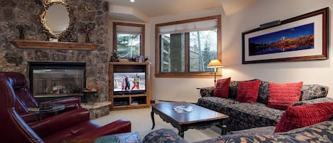 Settle into your cozy living room with a crackling stone fireplace, plush seating, and mountain artwork that captures the alpine spirit all around you.