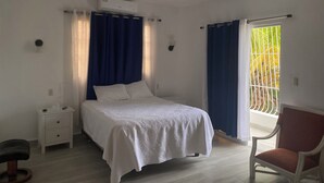 Un dormitorio con cama, mesita de noche, silla, ventilador de techo y ventana con cortinas.