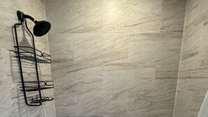 Ein Badezimmer mit einer weißen Badewanne, einem schwarzen Handtuch und einer an der Wand befestigten Duschbrause.