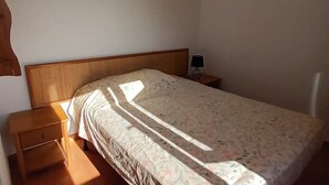 A single bed with a wooden headboard, a nightstand with a lamp, and a small drawer unit. - Exceptional stay in Corsica - Air-conditioned apartment with sea view in Bravone (Linguizzetta)