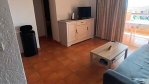 A living room with a sofa, a TV on a cabinet, a trash bin, and a small table. - Exceptional stay in Corsica - Air-conditioned apartment with sea view in Bravone (Linguizzetta)