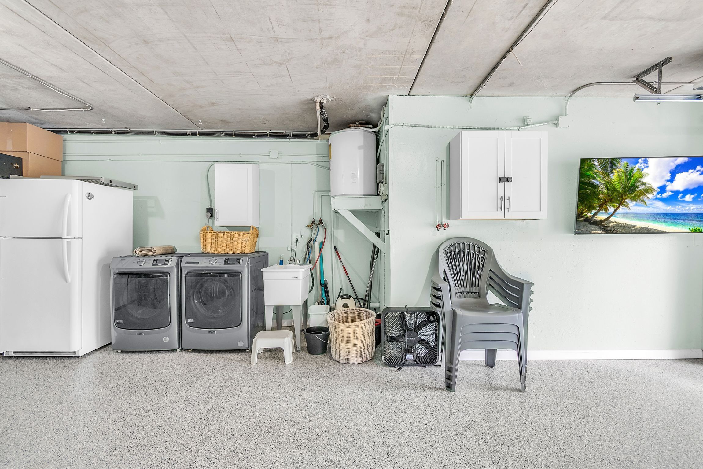 Ein Waschraum mit Waschmaschine, Trockner, Kühlschrank und Fernseher an der Wand.