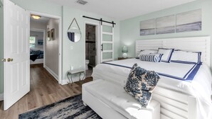 Un dormitorio con una cama grande, una mesita de noche, un espejo y una puerta que da a otra habitación.