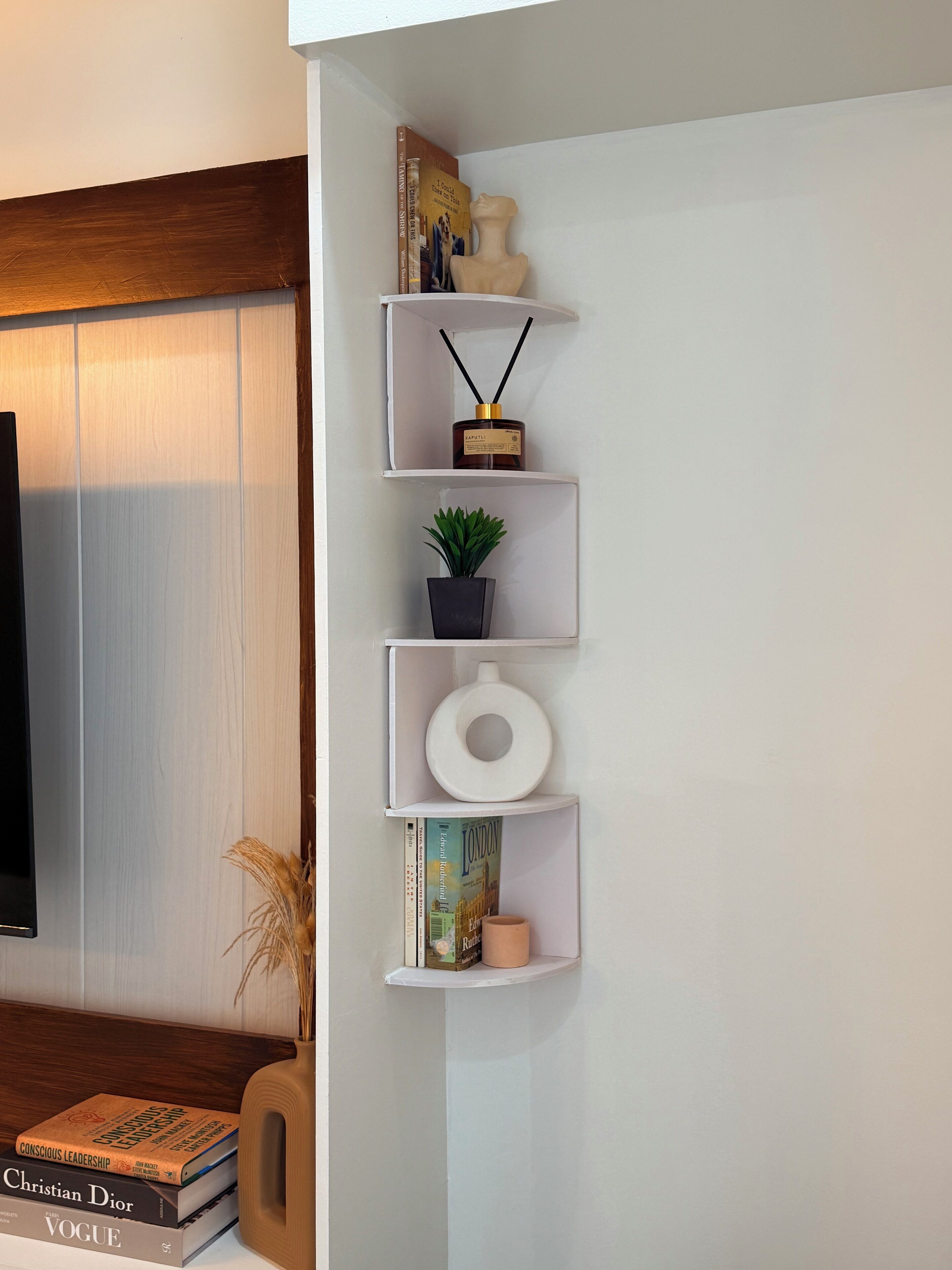 Pared blanca con una estantería empotrada que contiene libros, una pequeña planta en maceta, una vela y un adorno.