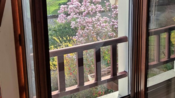 Et værelse med et stort vindue, der vender ud mod en have med lyserøde blomster og gelænder i træ.