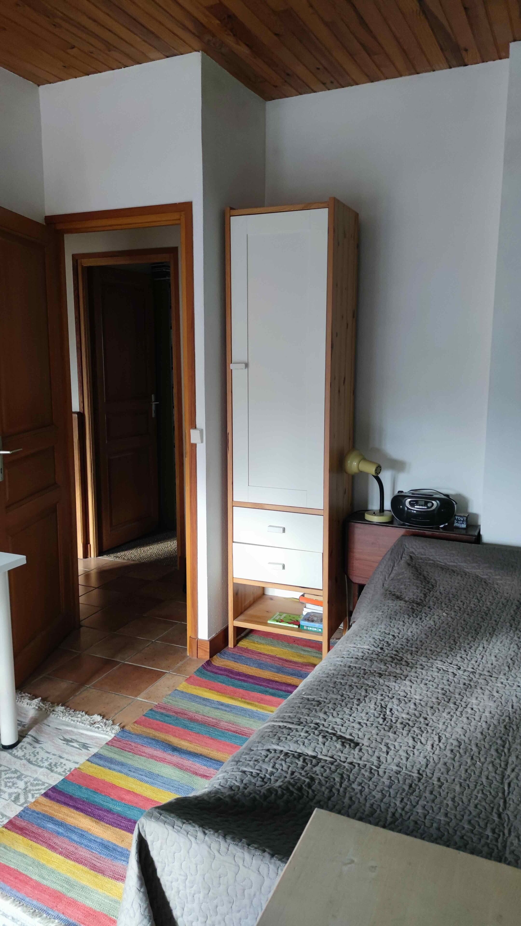 Een kamer met een bed, een kledingkast, een radio en een deur die naar een andere kamer leidt.