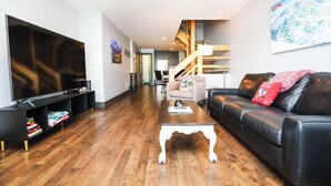 A modern living room with a flat-screen TV, a black leather sofa, a wooden coffee table, and a staircase leading to an upper level. - Eagle's Nest |3 Bedroom | Free Shuttle| Garage | Shared Hot Tub |  Mtn Views (Mt. Crested Butte)