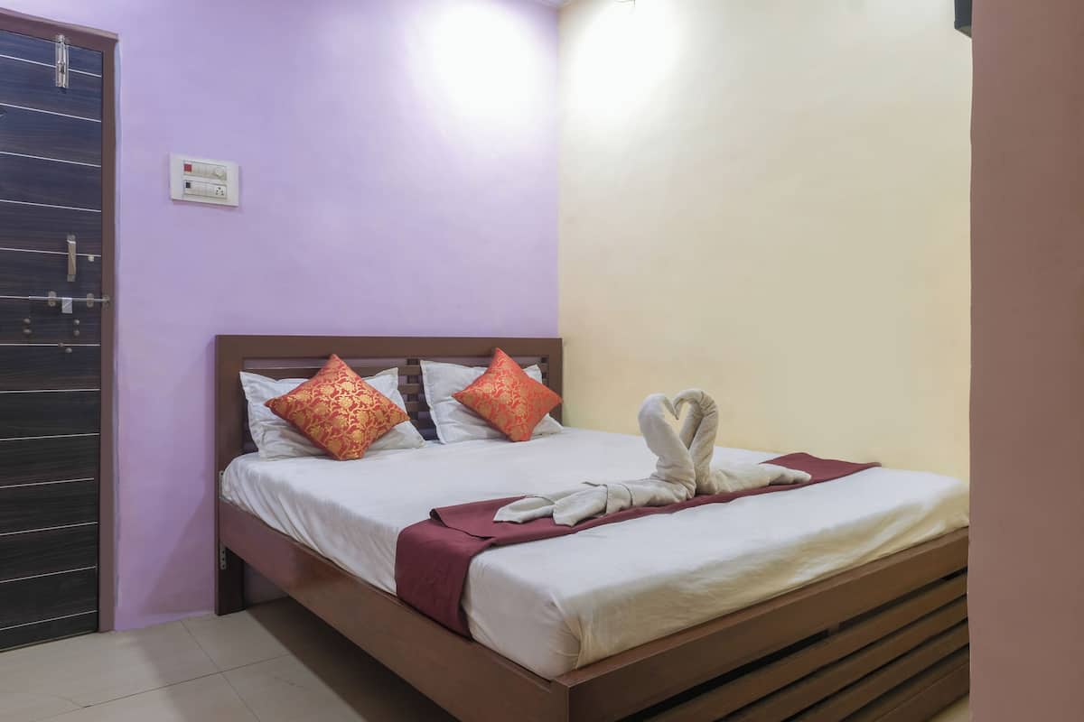 A neatly made bed with white linens, two red patterned pillows, and a towel arrangement on the side.