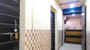 A hallway with a checkered floor pattern, a reception desk, and a door with a metal handle. - Amrapali Hotel (Bhiwandi)