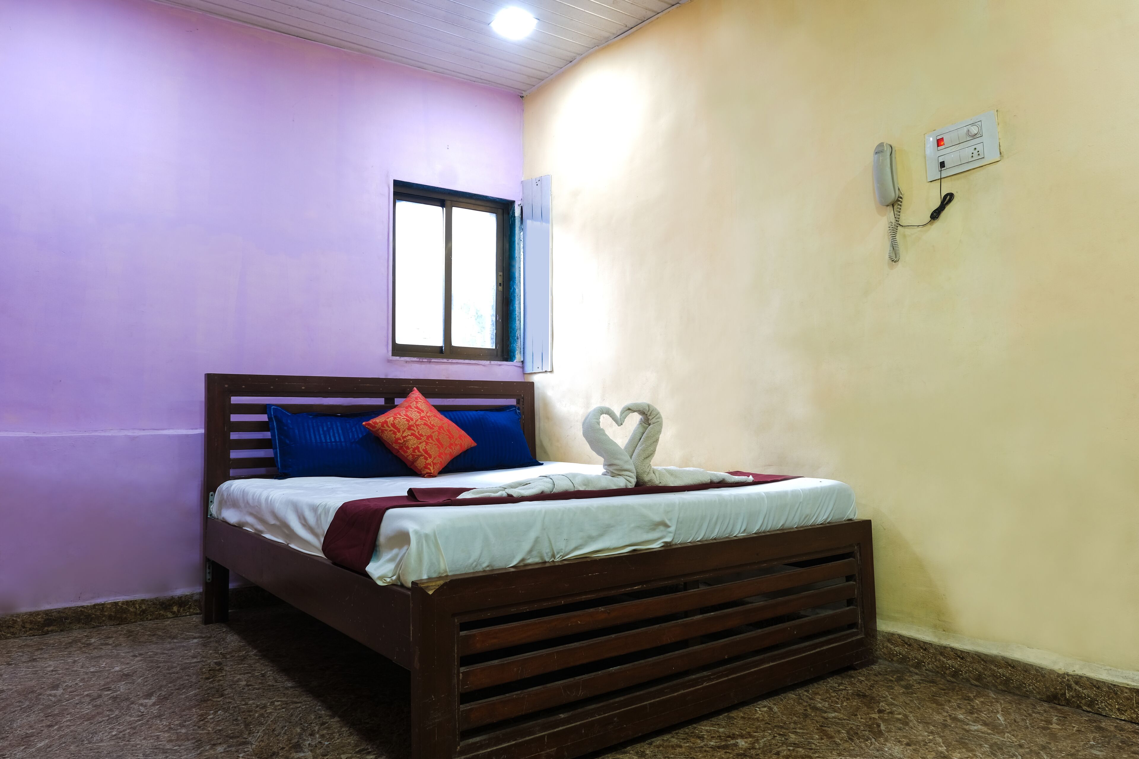 Une chambre avec un lit, une fenêtre et un téléphone fixé au mur.