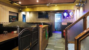 A restaurant interior with a wooden counter, ceiling fans, a TV, and a tiled floor. - Amrapali Hotel (Bhiwandi)
