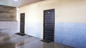A hallway with two doors, each with a metal handle and a small vent on the floor. The walls are tiled in a light and dark pattern. - Amrapali Hotel (Bhiwandi)