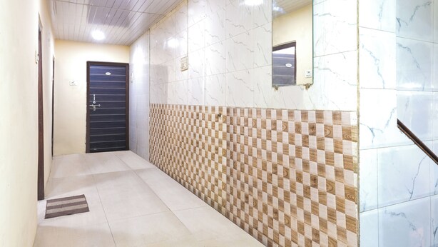 A hallway with a checkered wall pattern, a marble-tiled wall, and a door with a metal gate. - Amrapali Hotel (Bhiwandi)
