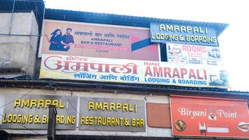Diversos sinais indicando o alojamento e o restaurante AMRAPALI, incluindo um sinal de hotel e um anúncio do Biriyani Point.
