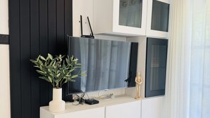 Ein modernes Wohnzimmer mit einem Flachbildfernseher, der an einem weißen Schrank befestigt ist, einer Topfpflanze und einer Holzskulptur.