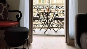 Habitación con vistas a un edificio a través de una puerta de cristal, una pequeña mesa con sillas, un sillón rojo y un sofá.