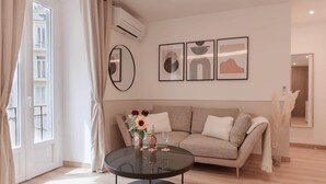 Ett modernt vardagsrum med ett runt glasbord, en beige soffa och abstrakt väggkonst.