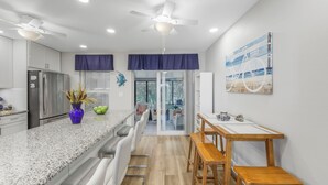 A modern kitchen with a granite countertop, white cabinets, a stainless steel refrigerator, and a dining area with a wooden table and chairs. - Centrally located townhouse w/ heated pool & spa (Marco Island)