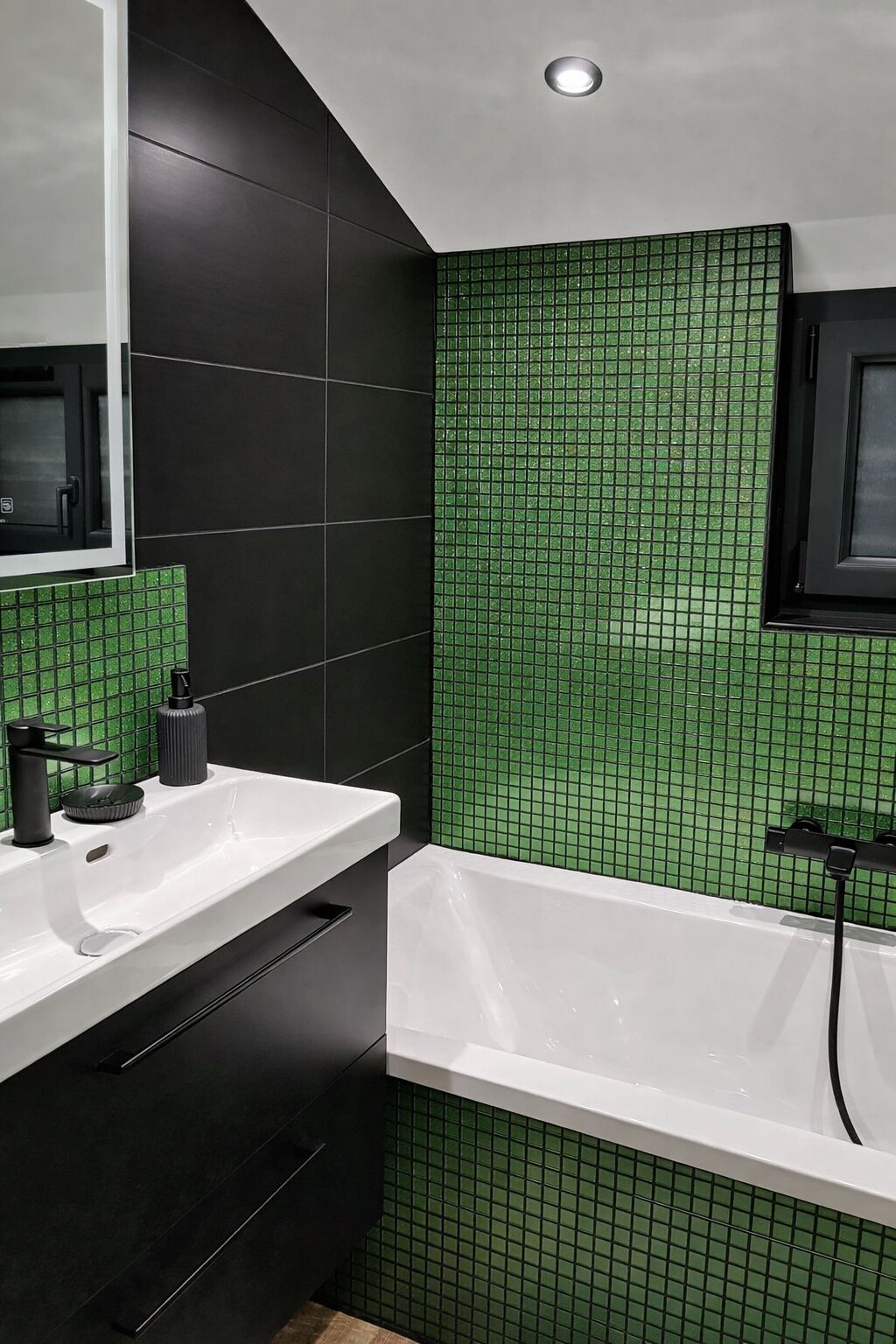 Un baño moderno con pared de azulejos negros y verdes, un lavamanos blanco y una bañera.